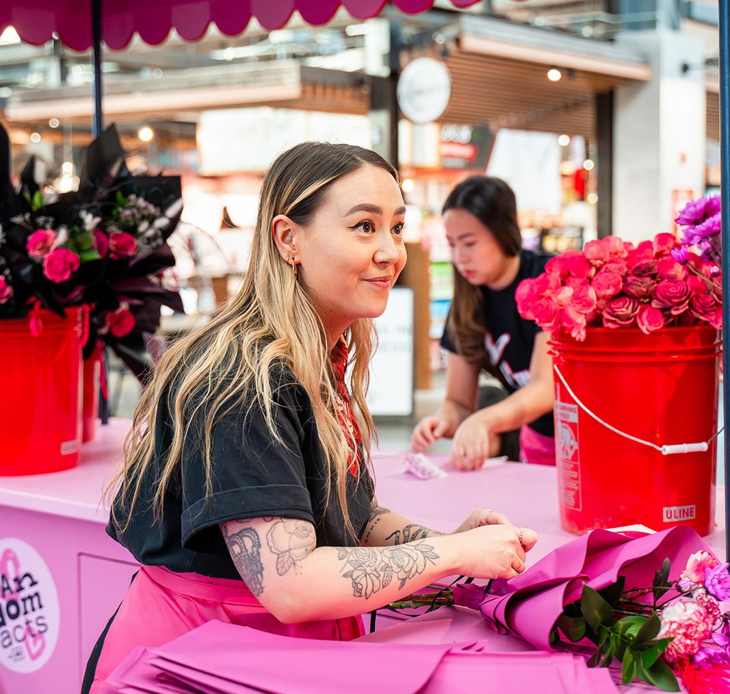 A cheerful Random Acts ambassador wraps a bouquet in a pink pop-up floral boutique.
