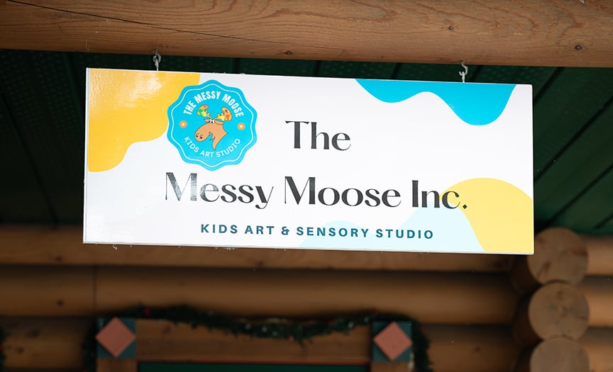 The forest green front door of The Messy Moose, set into a charming log cabin.