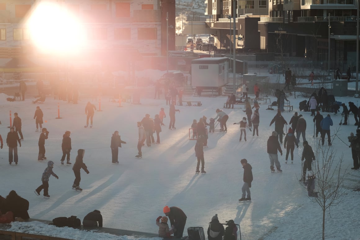 An outdoor skating rink packed with Calgarians of all ages, bathed in the dreamy rays of the winter sun. On the left side, people participate in a sledge hockey demonstration. 